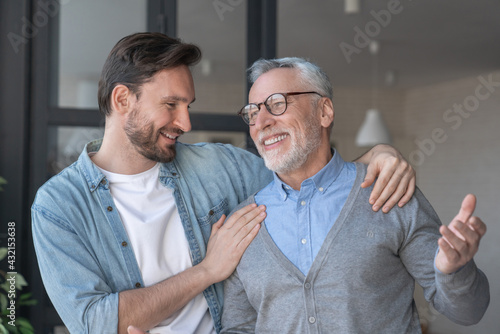 Fotografie Young adult caucasian son listening and supporting his old elderly senior father at home indoors