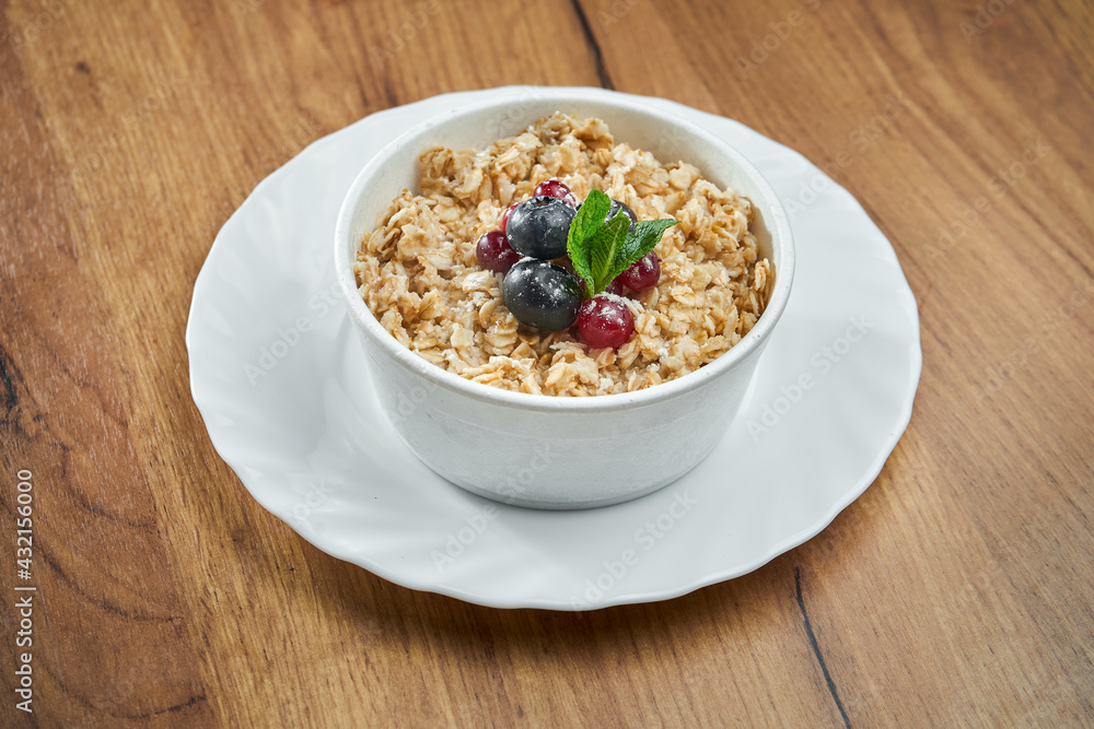 Appetizing oatmeal in milk with berries in a white bowl on a wooden background.