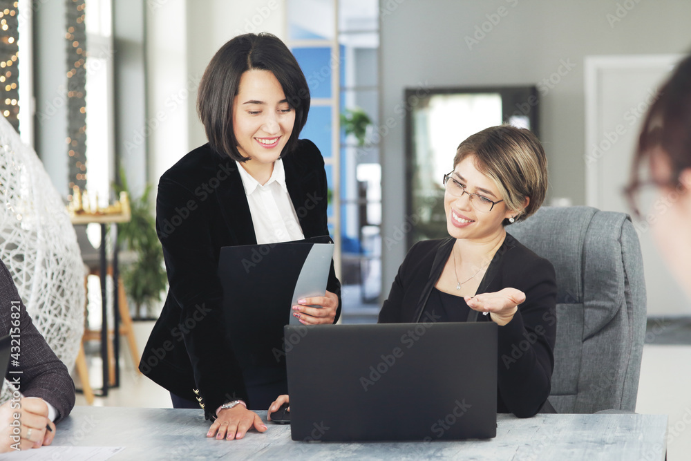 Two young business women in the office, analyzing information looking into a laptop and smiling Two young business women in the office, analyzing information looking into a laptop and smiling