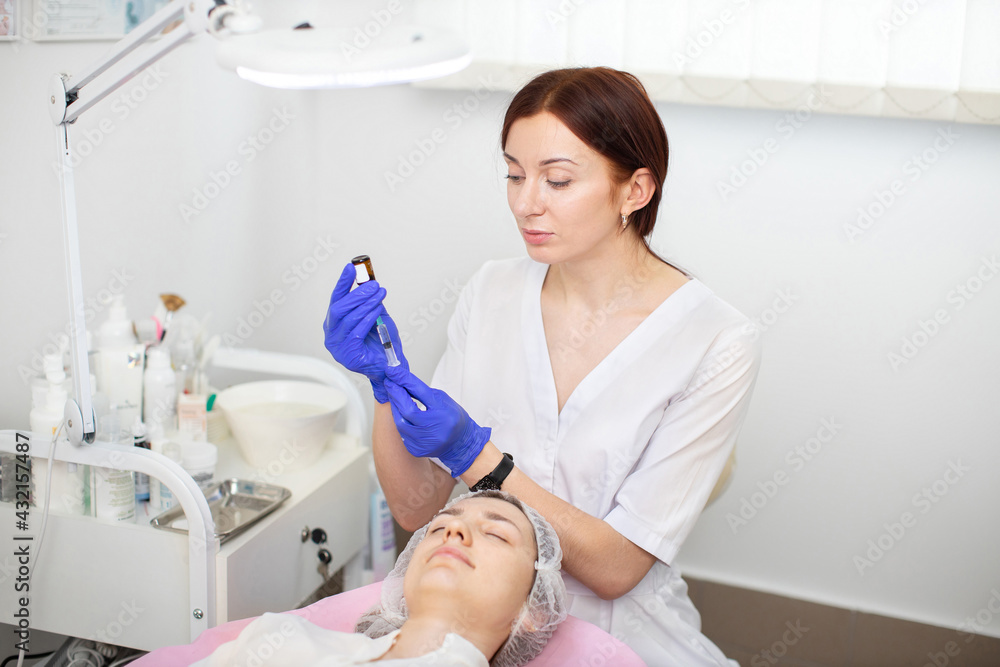 Facial anti wrinkle therapy in wellness center. Beautiful caucasian woman doctor dermatologist holds bottle with treatment oil or serum for skin rejuvenation. Woman patient lying on the couch Facial anti wrinkle therapy in wellness center. Beautiful caucasian woman doctor dermatologist holds bottle with treatment oil or serum for skin rejuvenation. Woman patient lying on the couch