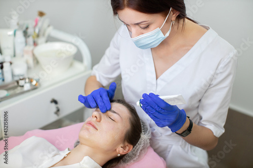 Dermatology treatment. Perfect skin concept. Woman cosmetologist applying cream with essential vitamins on face of young lady to improve client skin. Health, skin care, aesthetic medicine concept.
