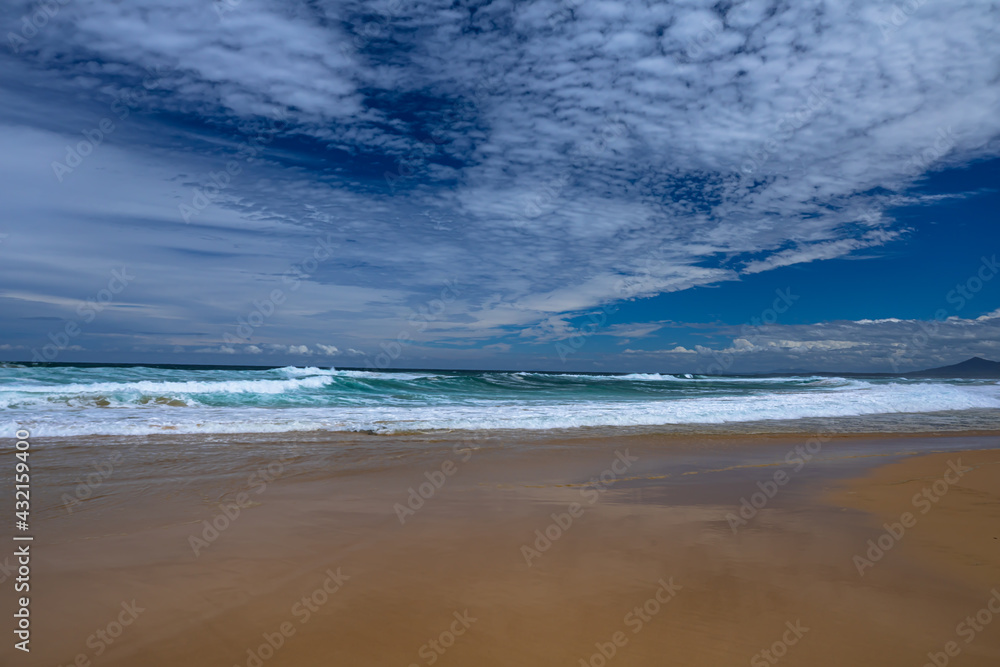 Landscape sandy beach with a beautiful series of cloud patterns and types of reflections on the beach and surf waves from the bright afternoon sunlight on the east coast of Australia. Landscape sandy beach with a beautiful series of cloud patterns and types of reflections on the beach and surf waves from the bright afternoon sunlight on the east coast of Australia.