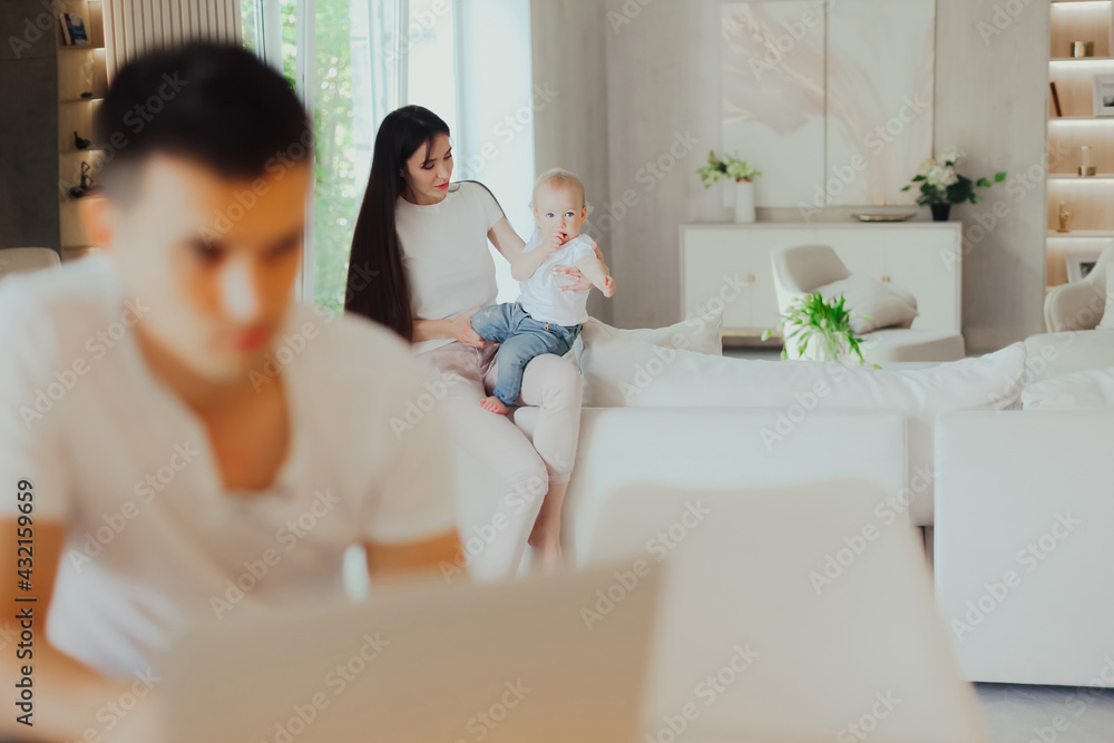 Young mother looks after her baby while her husband works on laptop Young mother looks after her baby while her husband works on laptop