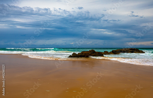 A view of a national park beach with smooth sand, beautiful turquoise water and white surf action framed by the dark clouds of a recent storm, located on the east coast of Australia.