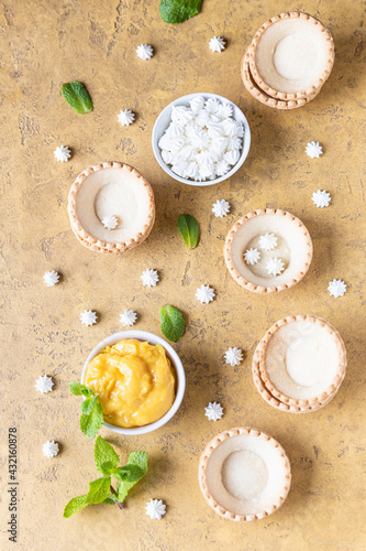 Empty shortbread tartlets, lemon curd, mini meringues and mint on concrete background. Process making dessert. Top view.
