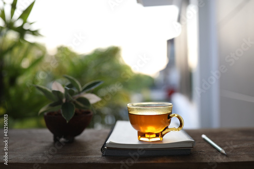 tea in clear transparent glass and notebooks with pencil on wooden table at outdoor