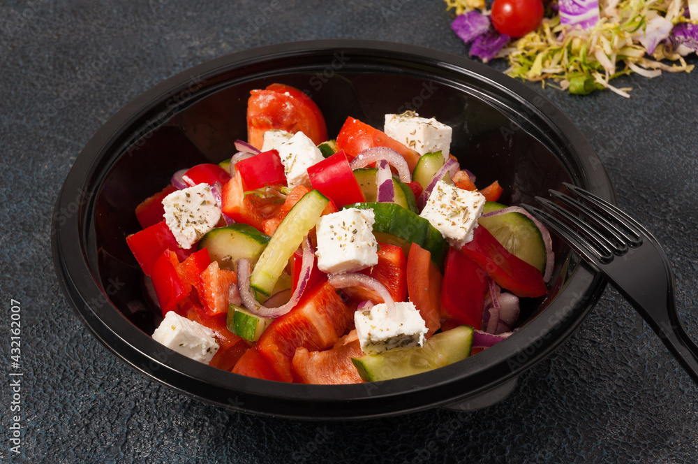 Greek salad in a black plastic bowl. Concept: food delivery