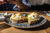 Two pieces of toasted whole rye bread with mashed avocado, poached eggs and sauce. Sandwiches with egg, avocado and sauce.