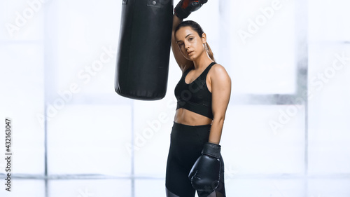 exhausted sportswoman in boxing gloves leaning on punching bag in gym. © LIGHTFIELD STUDIOS