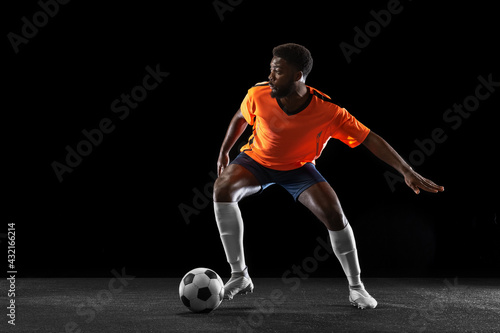 Young African football soccer player playing isolated on black background. Concept of sport, movement, energy and dynamic. © master1305
