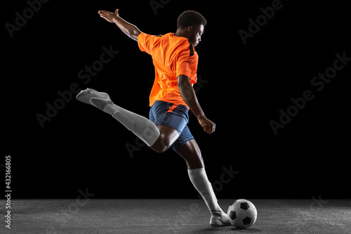 Young African football soccer player playing isolated on black background. Concept of sport.