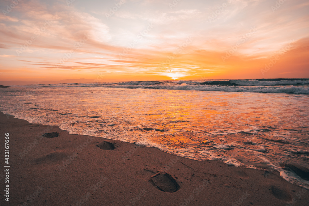 Footprints in the sand in front of the ocean during sunset, calm ocean and beautiful colorful sky, California Footprints in the sand in front of the ocean during sunset, calm ocean and beautiful colorful sky, California