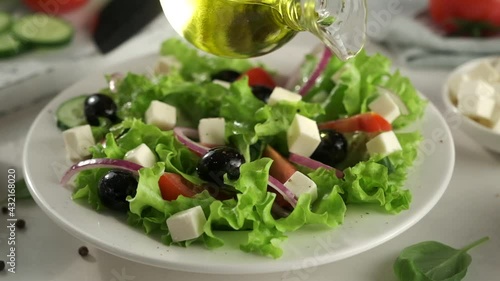 Greek salad of fresh cucumber, tomato, lettuce, red onion, feta cheese and olives with olive oil. Greek Salad Preparing. Olive Oil Pouring. Salad Dressing. Cooking. Healthy Food. Slow Motion Footage