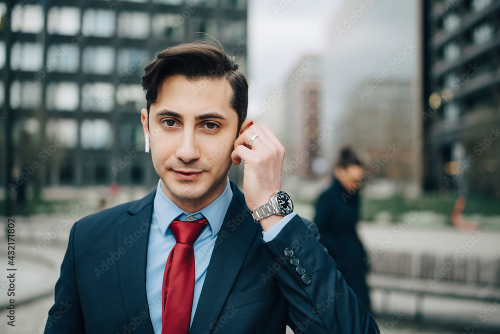 Confident businessman wearing wireless in-ear headphones at office park Confident businessman wearing wireless in-ear headphones at office park