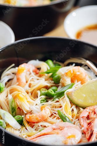 romantic dinner for two. Asian cuisine, rice noodles with shrimp and seafood, green peas and onions. soy sauce and various fresh vegetables. romantic dinner in black plates with Japanese chopsticks