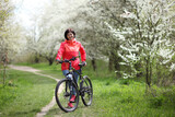 Beautiful woman on a bike in a blooming spring garden. Beautiful mature woman posing for the camera in a blooming spring garden.