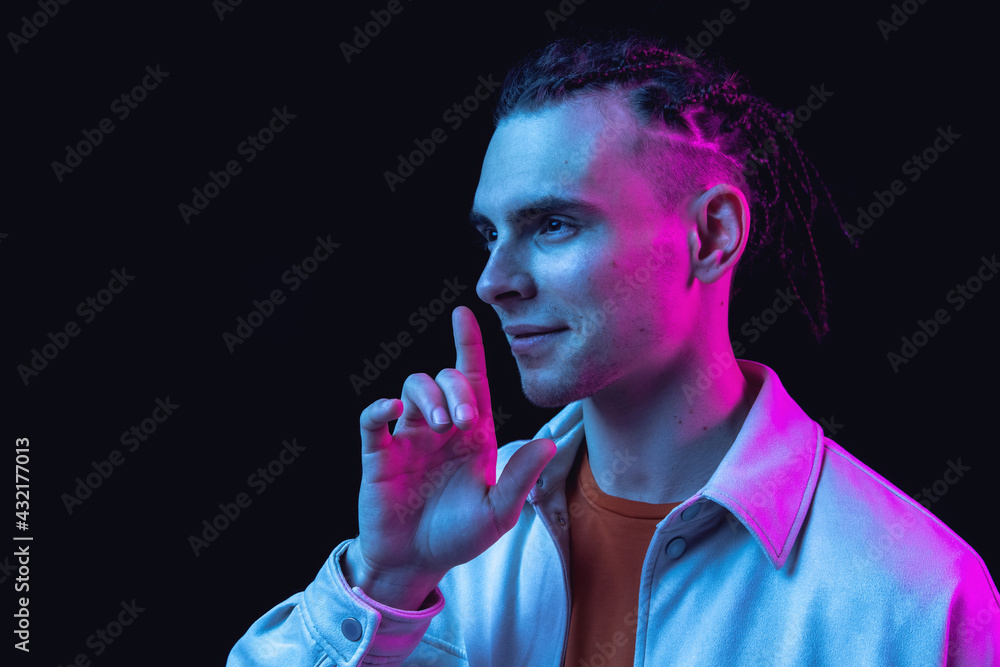 Caucasian young man's portrait on dark studio background in neon. Concept of human emotions, facial expression. Caucasian young man's portrait on dark studio background in neon. Concept of human emotions, facial expression.