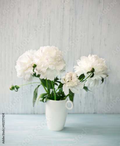 Garden white peonies  in a white porcelain vase  on a light blue wooden background, close up