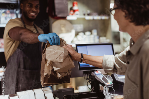 Male owner giving package order to female customer in delicatessen shop photo