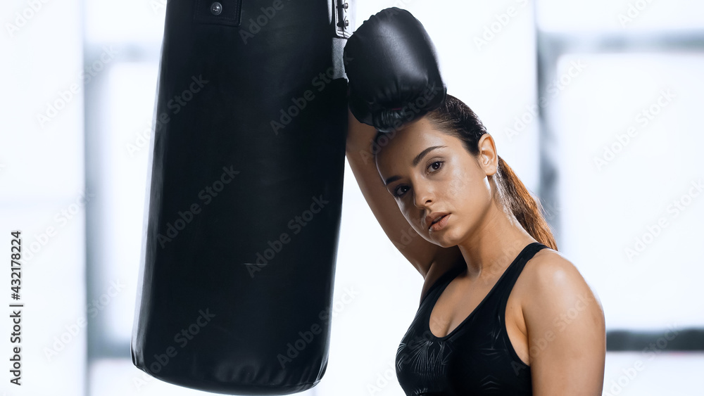 tired sportswoman in boxing glove resting while leaning punching bag in gym.