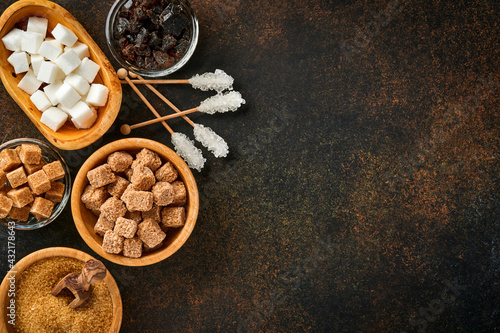 White sugar, cane sugar cubes, caramel in bamboo bowl on dark brown table concrete background. Assorted different types of sugar. Top view or flat lay.