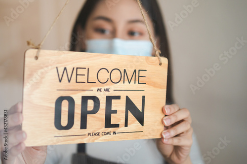 Reopen, asian young owner retail, coffee shop woman turning sign board open wearing face mask, protect to pandemic of coronavirus, reopen store after close lockdown quarantine in covid-19, new normal.