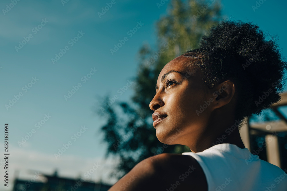 Confident sportswoman looking away in park on sunny day