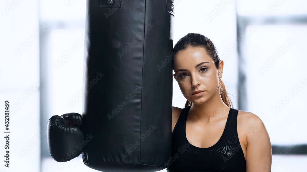 tired sportswoman in boxing glove resting near punching bag.