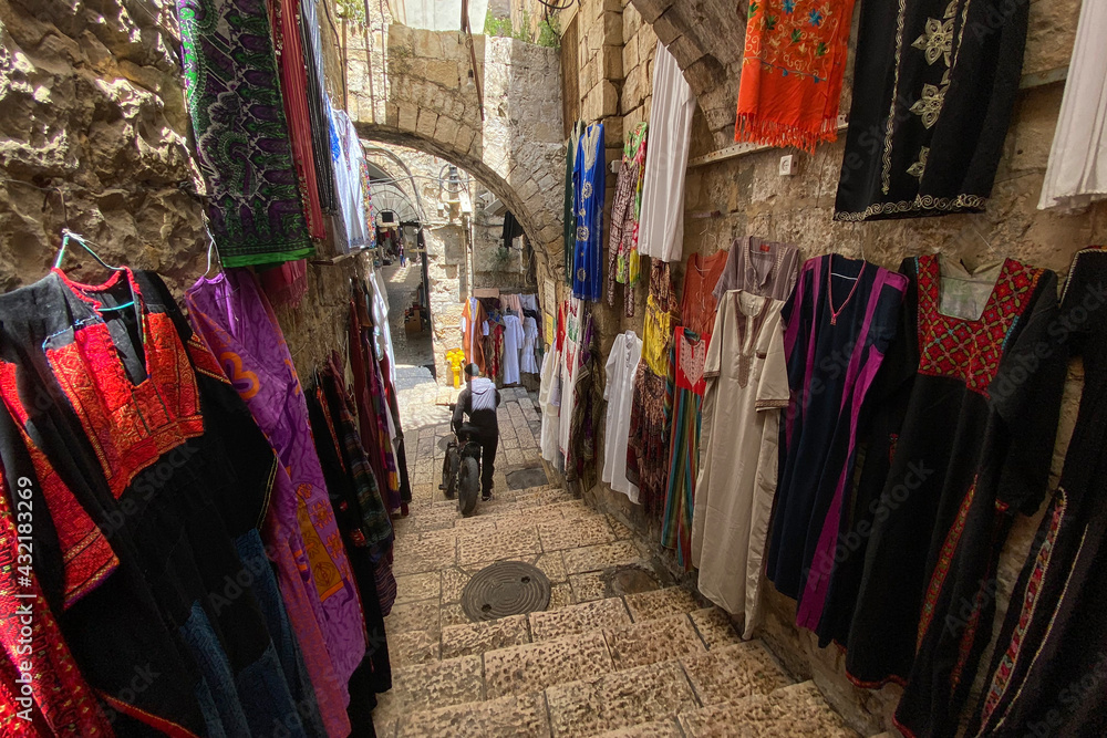 Narrow street of the Arab market in the old city if Jerusalem. National dresses are hung along the walls.