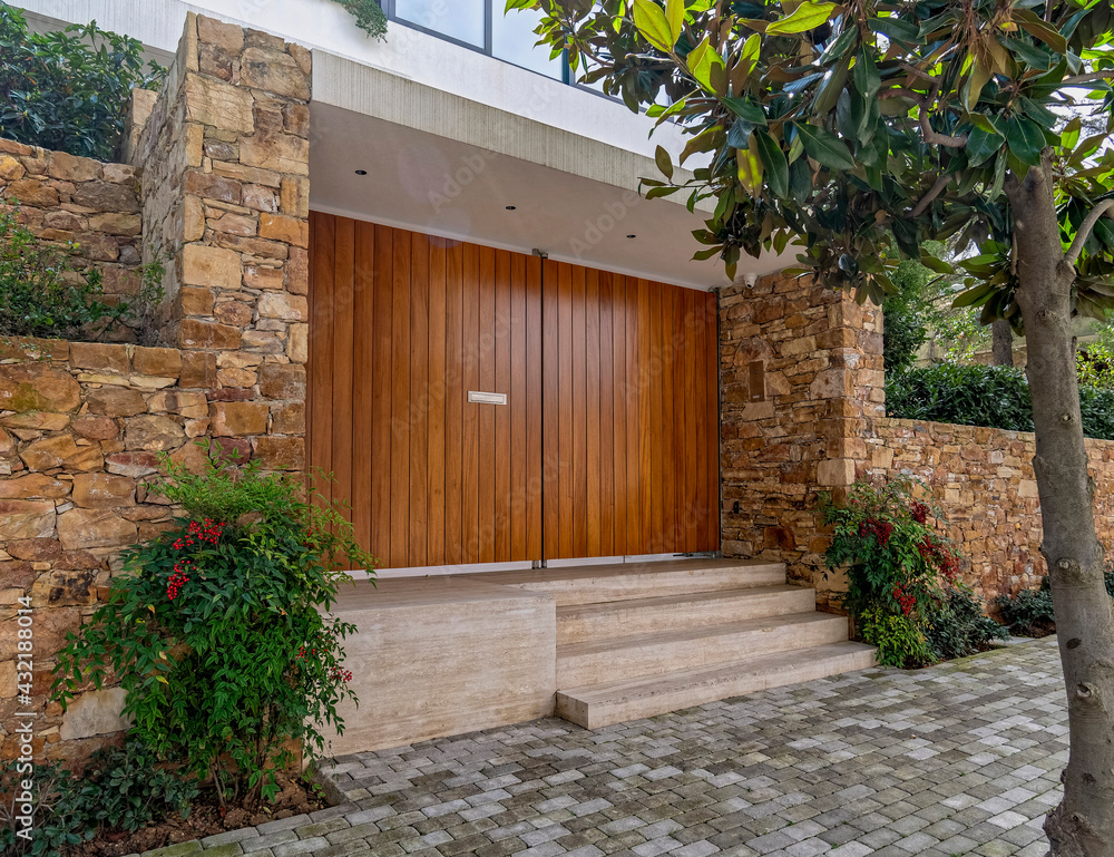 Fototapeta premium elegant house front huge entrance wooden door and stone fence with green plants, Athens Greece