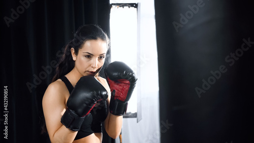 young woman in boxing gloves and sportswear training with punching bag in gym.