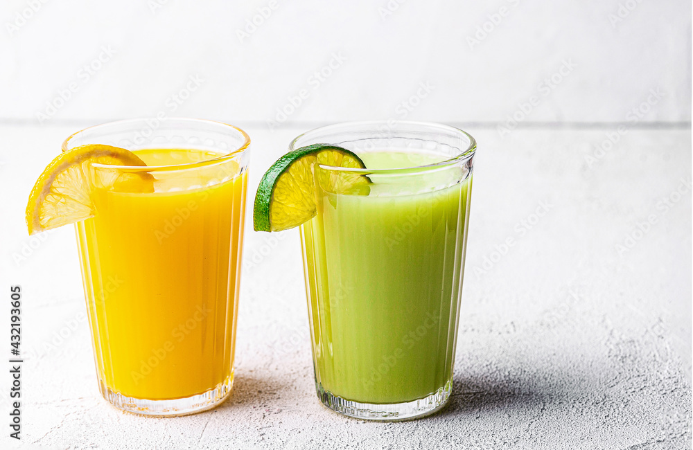 Two glasses of orange, kiwi and avocado smoothies, garnished with lemon wedges on a white table. Selective Focus. Front view Two glasses of orange, kiwi and avocado smoothies, garnished with lemon wedges on a white table. Selective Focus. Front view