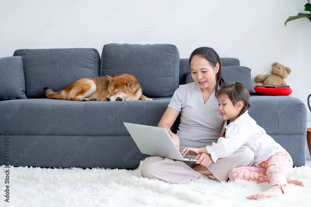 Asian woman and little girl enjoy together in living room by using laptop and sit on the floor while their shiba dog lie on sofa. Asian woman and little girl enjoy together in living room by using laptop and sit on the floor while their shiba dog lie on sofa.