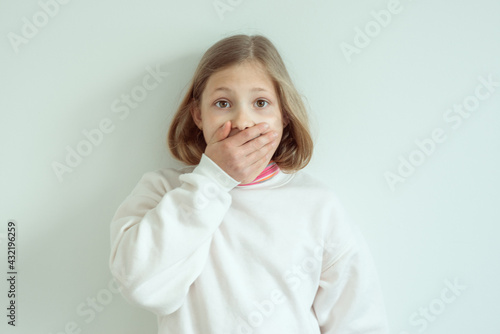 Amazed little girl with widely opend eyes shut her mouth with hand