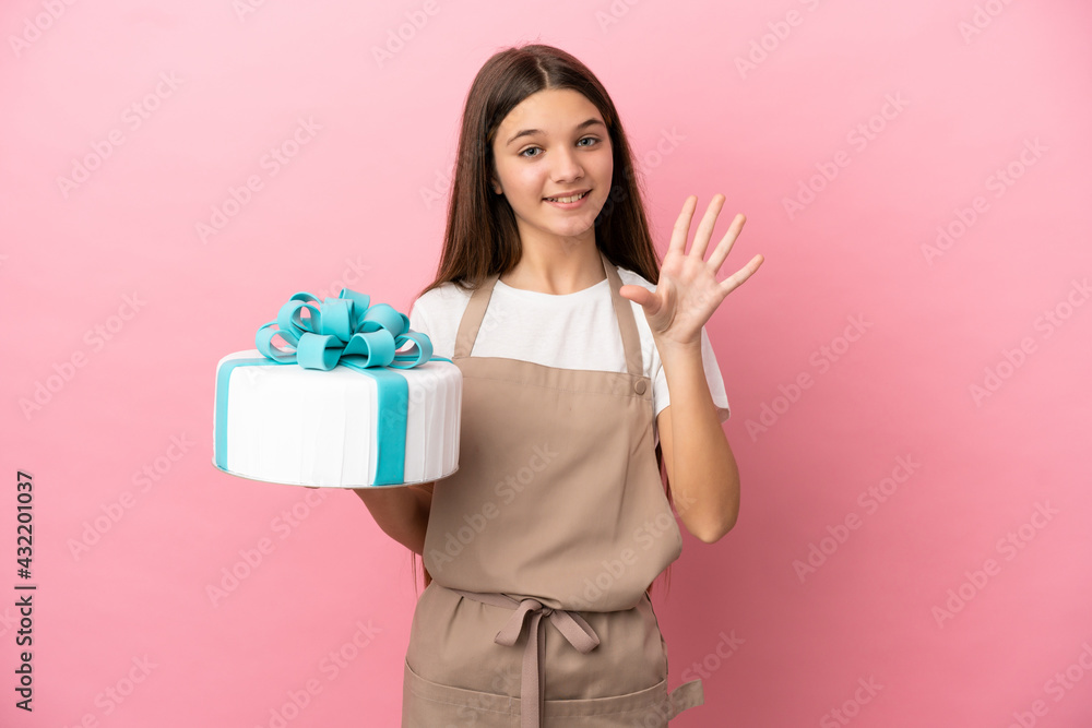 Little girl with a big cake over isolated pink background saluting with hand with happy expression