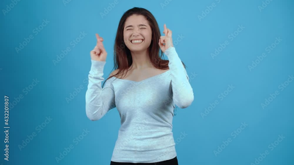 The beautiful, charismatic girl holds her fingers crossed in both hands, she hopes that the wish will come true. Asian with dark hair, dressed in a blue blouse, isolated on a dark blue background in The beautiful, charismatic girl holds her fingers crossed in both hands, she hopes that the wish will come true. Asian with dark hair, dressed in a blue blouse, isolated on a dark blue background in