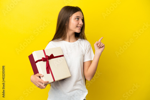Little girl holding a gift over isolated yellow background pointing up a great idea