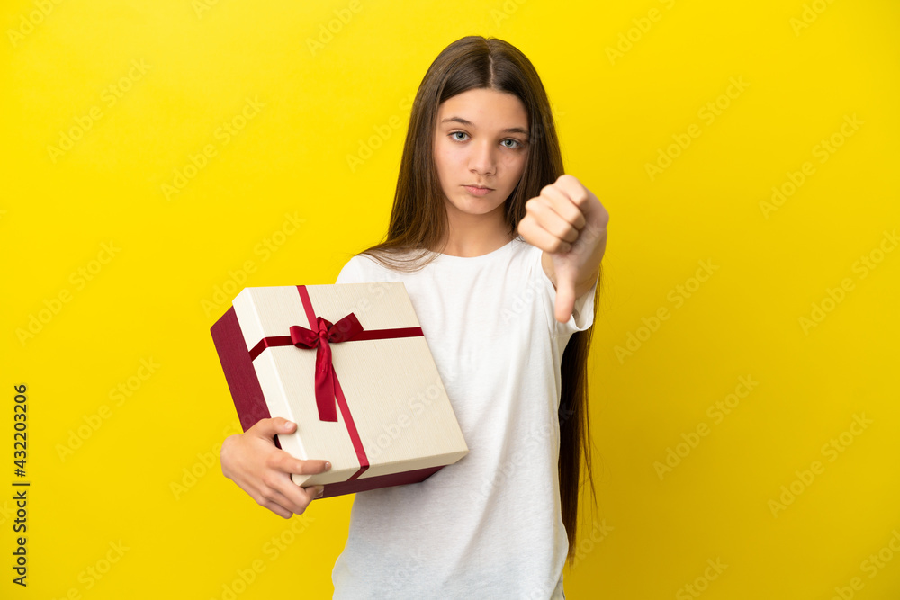 Little girl holding a gift over isolated yellow background showing thumb down with negative expression Little girl holding a gift over isolated yellow background showing thumb down with negative expression
