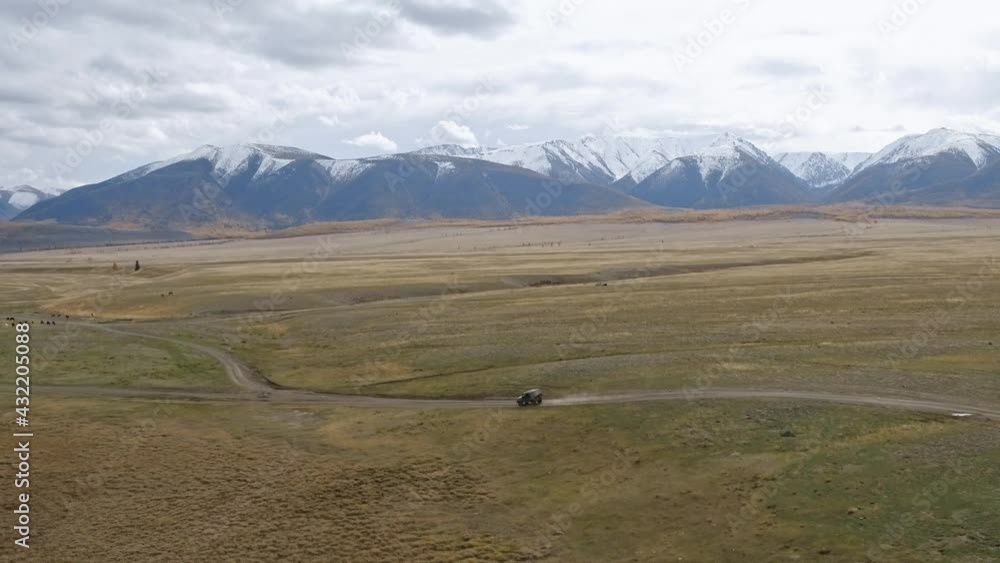 Aerial view of automobile riding along sandy road in dry mountainous valley on cloudy day. Dry Altay endless Landscape. Breathtaking Edge of the earth. 4k footage Aerial view of automobile riding along sandy road in dry mountainous valley on cloudy day. Dry Altay endless Landscape. Breathtaking Edge of the earth. 4k footage