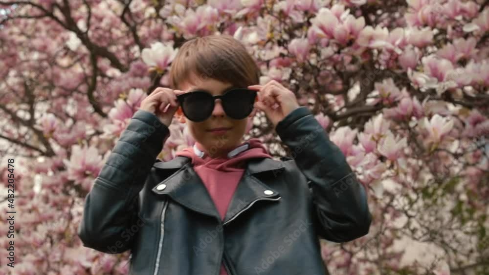Boy in glasses posing against a background of flowers of a tree. He makes body movements, looks around. Waiting for meeting. Boy in glasses posing against a background of flowers of a tree. He makes body movements, looks around. Waiting for meeting.