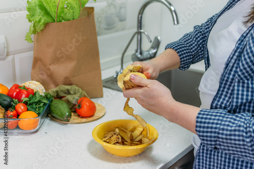 Food Loss and Food Waste. Reducing Wasted Food At Home. Solving the problem of Food waste. Female hands peeling potatoes, potato peel in a bowl photo