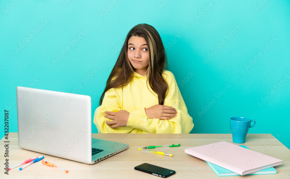 Little girl in a table with a laptop over isolated blue background making doubts gesture while lifting the shoulders Little girl in a table with a laptop over isolated blue background making doubts gesture while lifting the shoulders