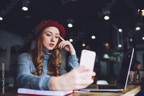 Calm female freelancer using phone and looking at screen in cafe