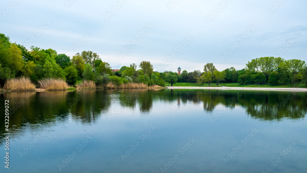 Panoramic landscape at lake in spring, green trees and blue sky symmetrically reflected in water