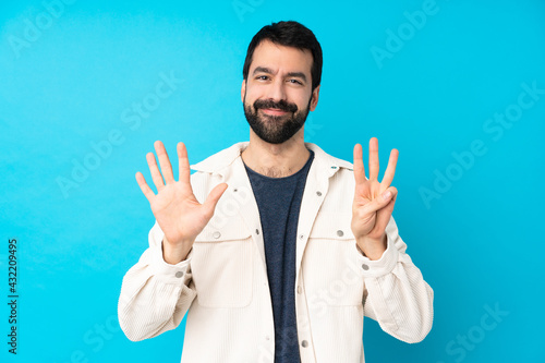 Young handsome man with white corduroy jacket over isolated blue background counting eight with fingers © luismolinero