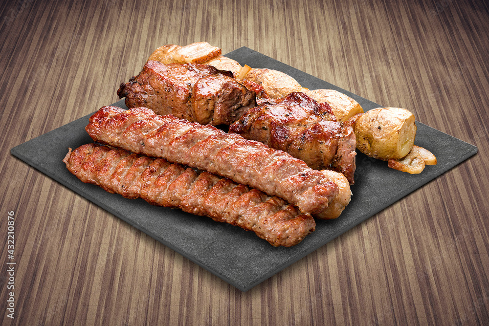 A selection of various barbecued gourmet meats on a black board with a rustic timber background. Pork kebab, lyulya, potatoes.