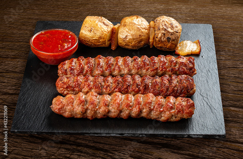 Stone board with different tasty cooked meat on wood background. Chicken kebab with baked potatoes