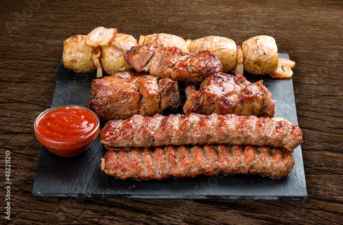 Stone board with different tasty cooked meat on wood background. Pork kebab, lyulya, potatoes.