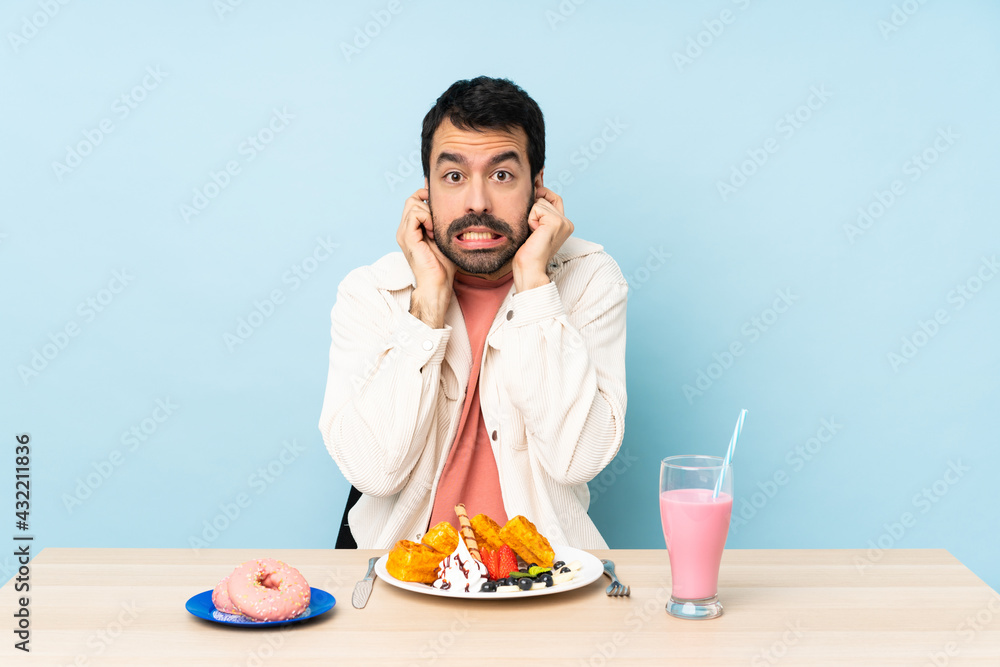 Man at a table having breakfast waffles and a milkshake frustrated and covering ears Man at a table having breakfast waffles and a milkshake frustrated and covering ears