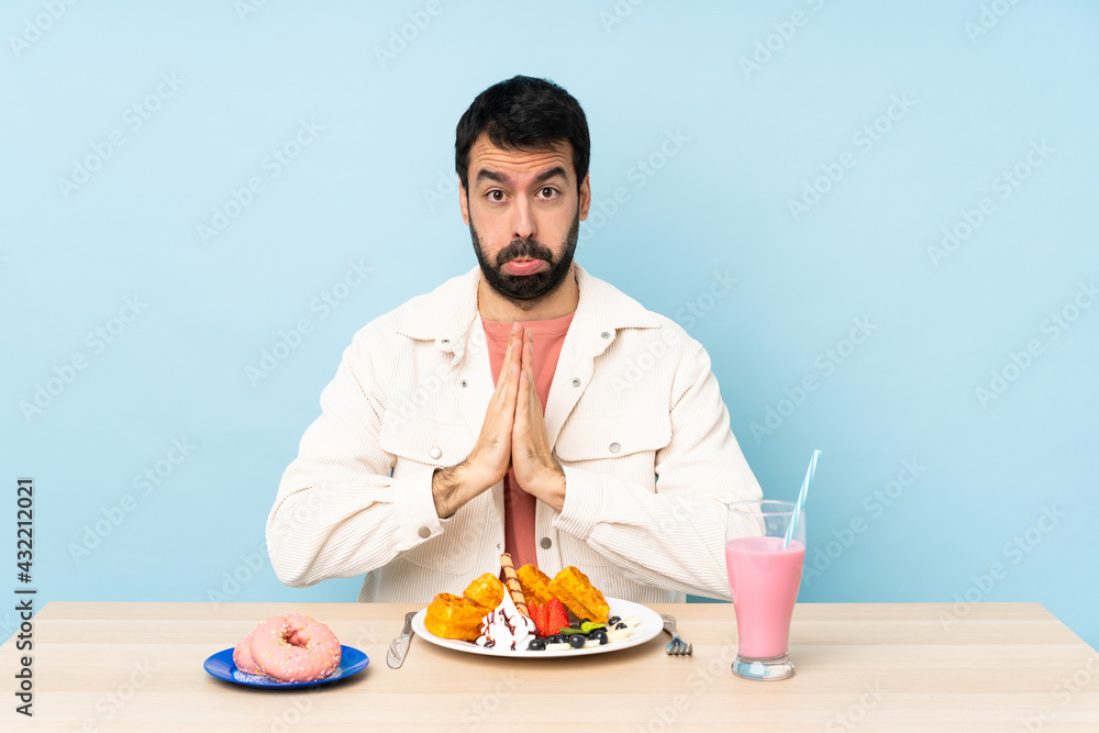 Man at a table having breakfast waffles and a milkshake keeps palm together. Person asks for something Man at a table having breakfast waffles and a milkshake keeps palm together. Person asks for something